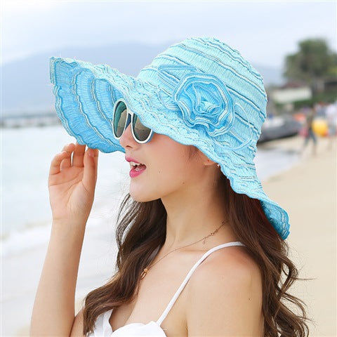 A woman wearing a Rippled Colored Flower Beach Hat and sunglasses on the beach.
