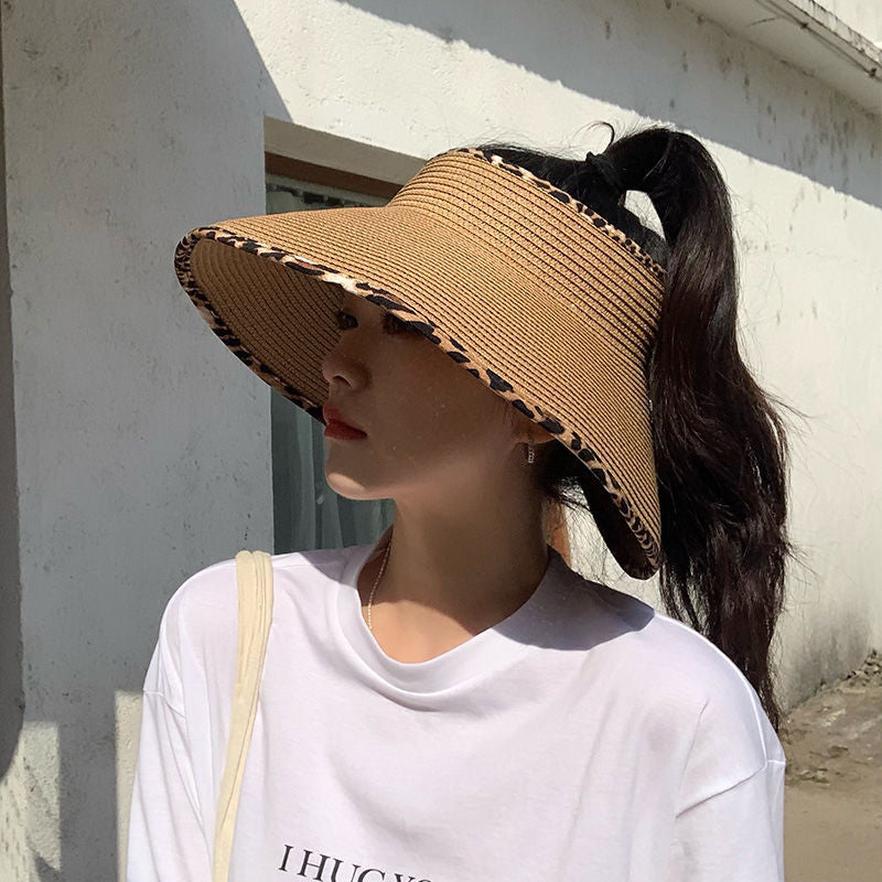 A woman wearing a Big Brim Cheetah Print Edge Straw Visor by Beachy Cover Ups with a ponytail.